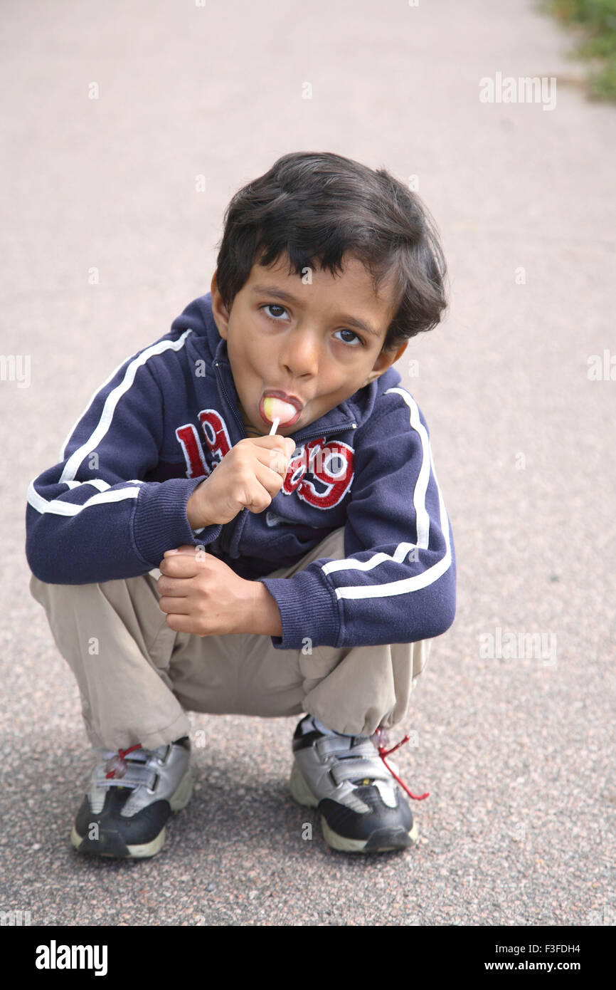Small four years old boy sitting on road and chewing eating lollipop MR#468 Stock Photo