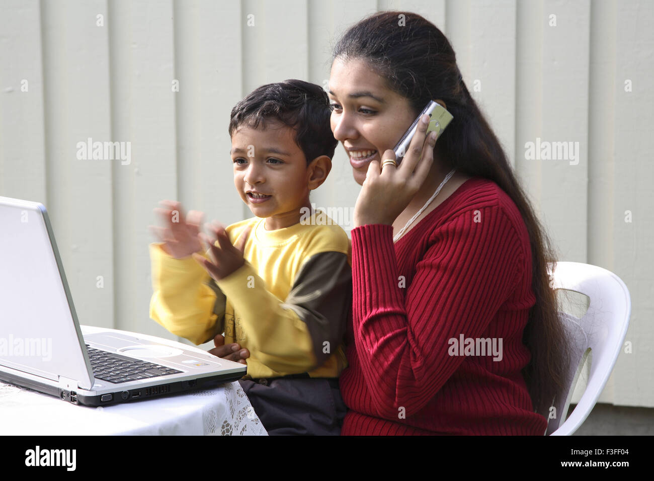 Mother speaking on mobile and boy clapping sitting in front of laptop MR#468 Stock Photo