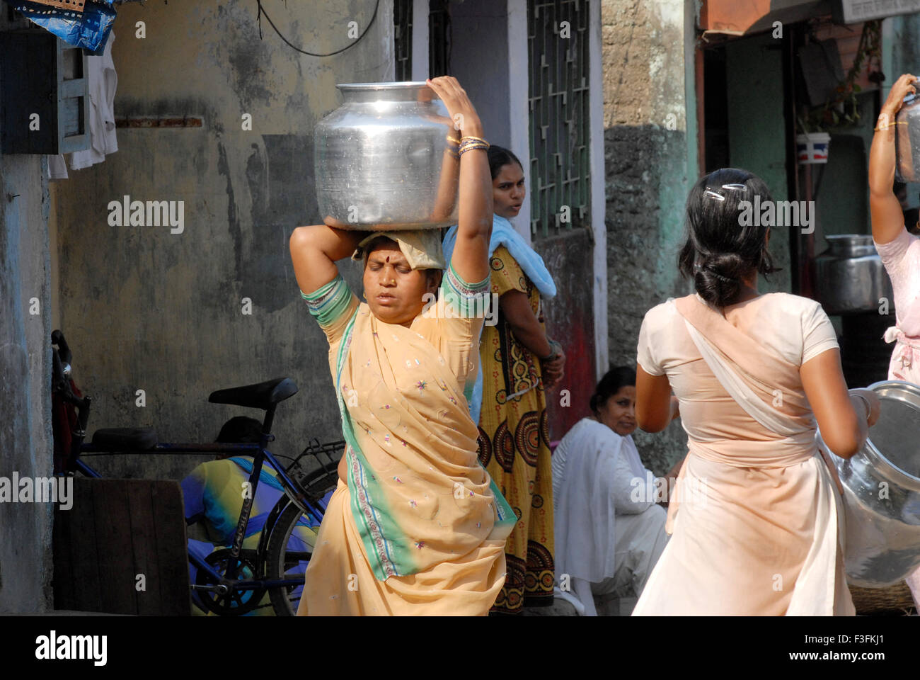 Women carry drinking water in aluminum containers on their heads at a slum in Chembur ; Bombay now Mumbai ; Maharashtra ; India Stock Photo