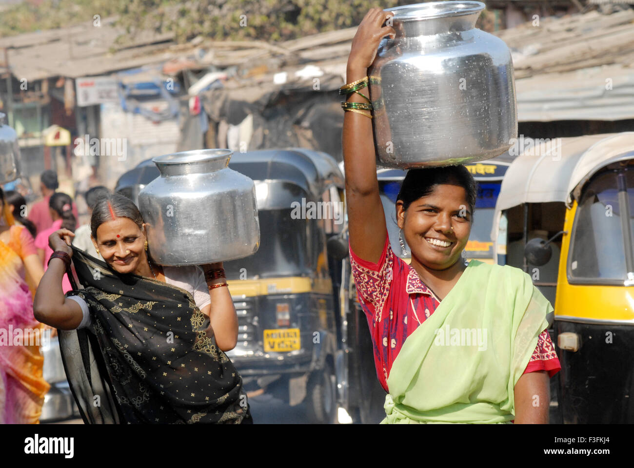 Women carry drinking water in aluminum containers on their heads at a slum in Chembur ; Bombay now Mumbai ; Maharashtra ; India Stock Photo