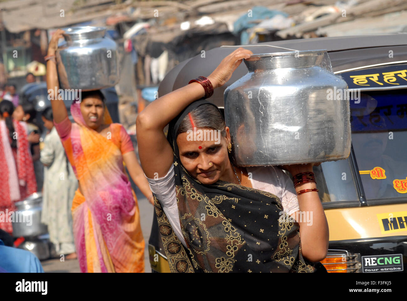 Women carry drinking water in aluminum containers on their heads at a slum in Chembur ; Bombay now Mumbai ; Maharashtra ; India Stock Photo