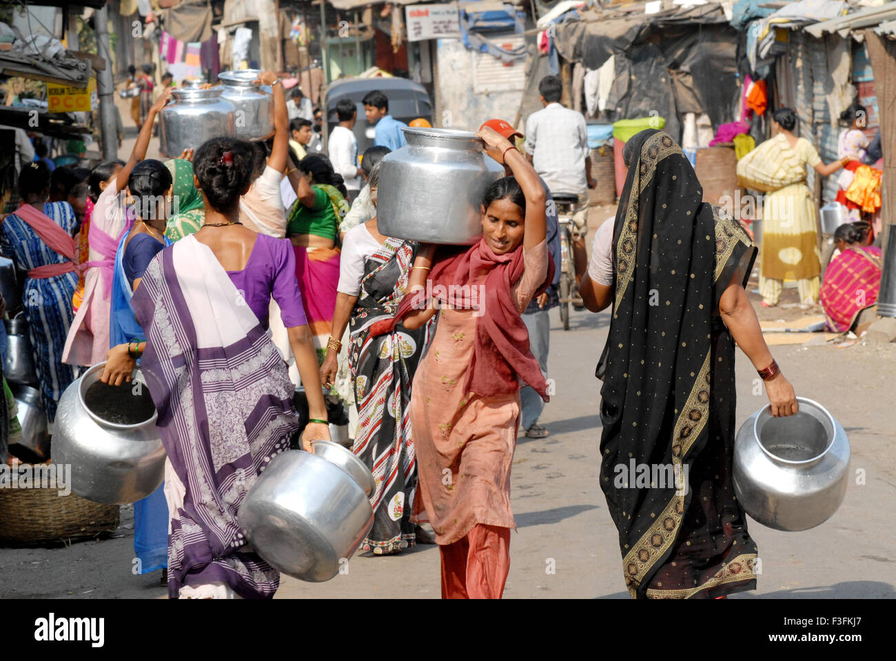 Women carry drinking water in aluminum containers on their heads at a slum in Chembur ; Bombay now Mumbai ; Maharashtra ; India Stock Photo