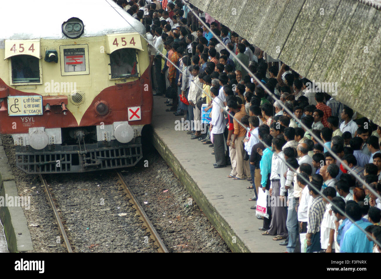 Commuters try to get into crowded local train during peak hour at Ghatkopar Railway Station in Bombay Mumbai Stock Photo