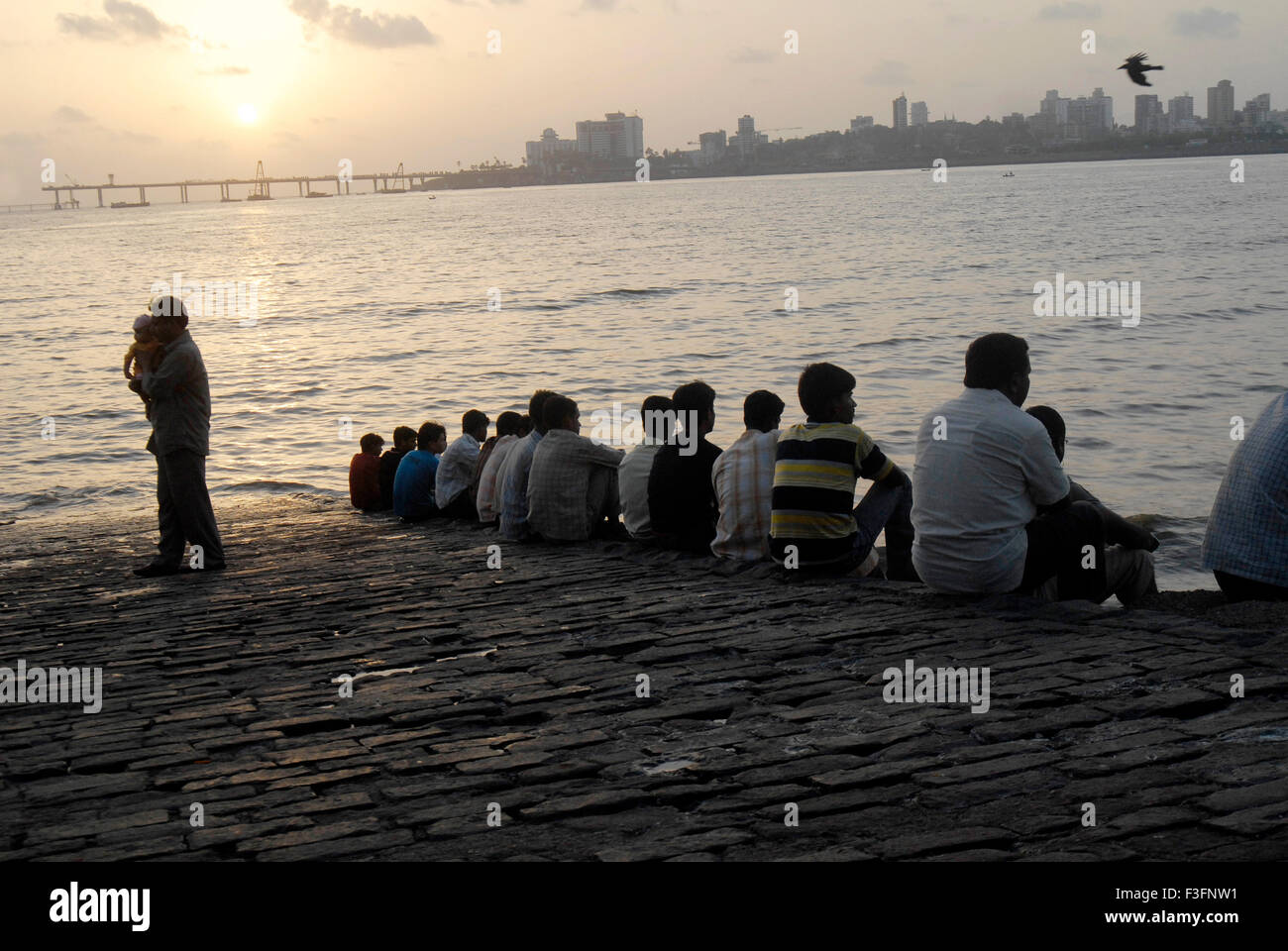 People sit in line enjoying cool sea breeze at Mahim beach on Arabian Sea in Bombay Mumbai ; Maharashtra ; India Stock Photo