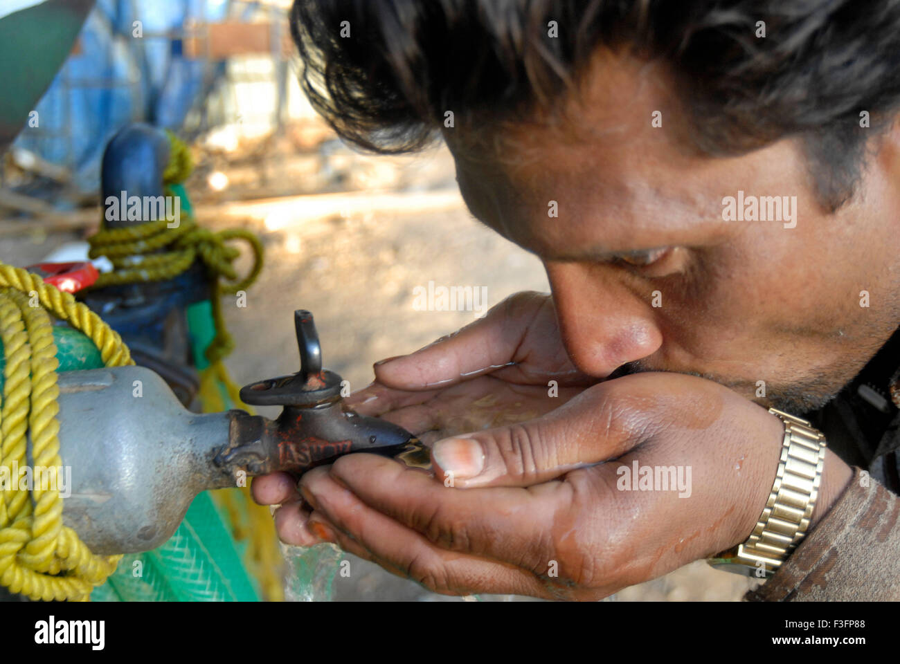 Man quenches his thirst by drinking water for tap ; Bombay Mumbai ; Maharashtra ; India Stock Photo