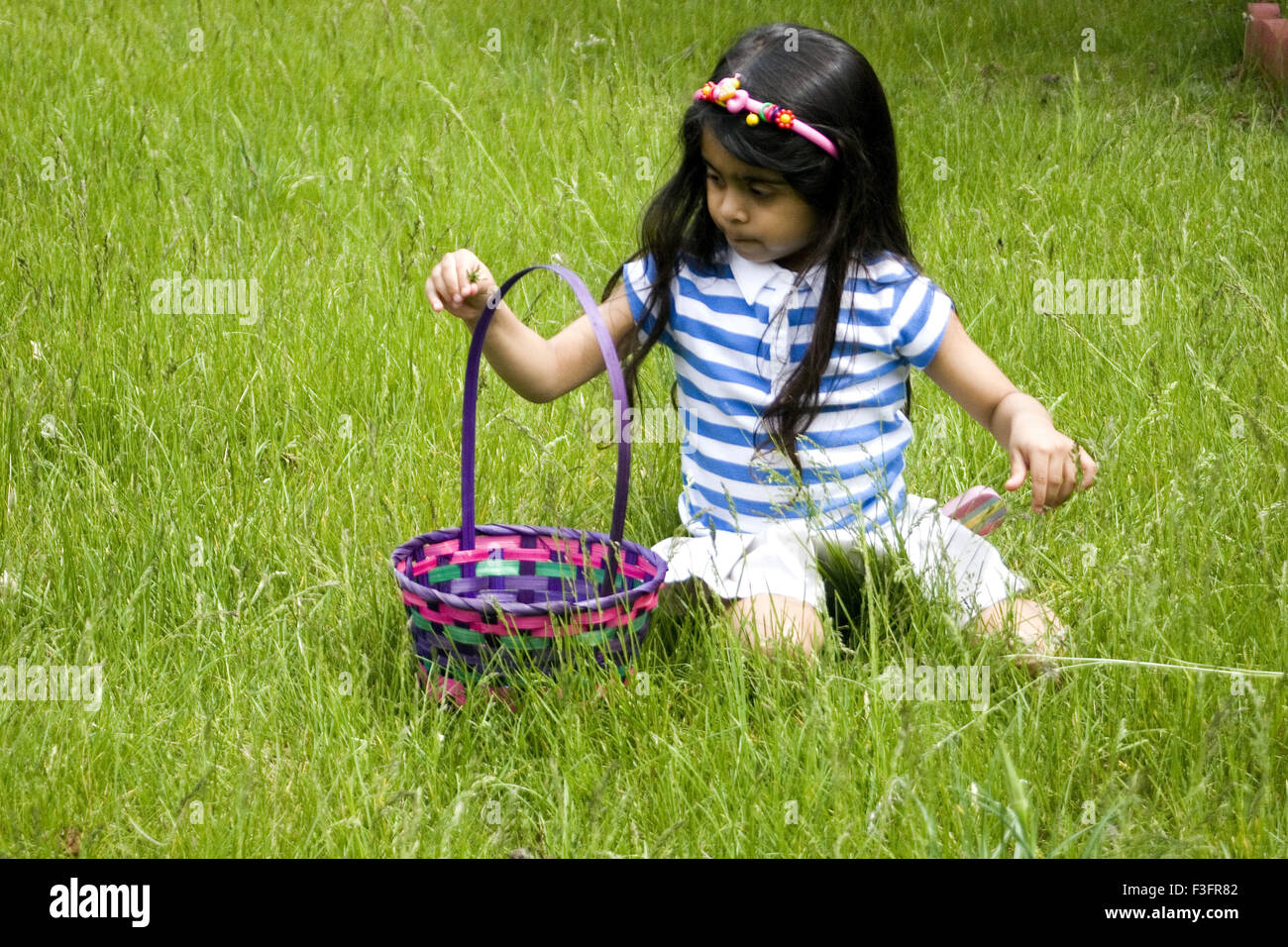Four years old girl busy on lawn trying to pick flowers Stock Photo