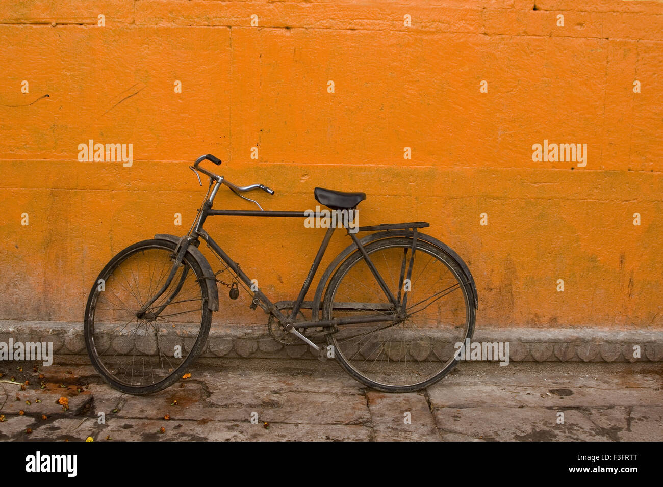 old bicycle parked against orange background wall ; India ; asia Stock Photo