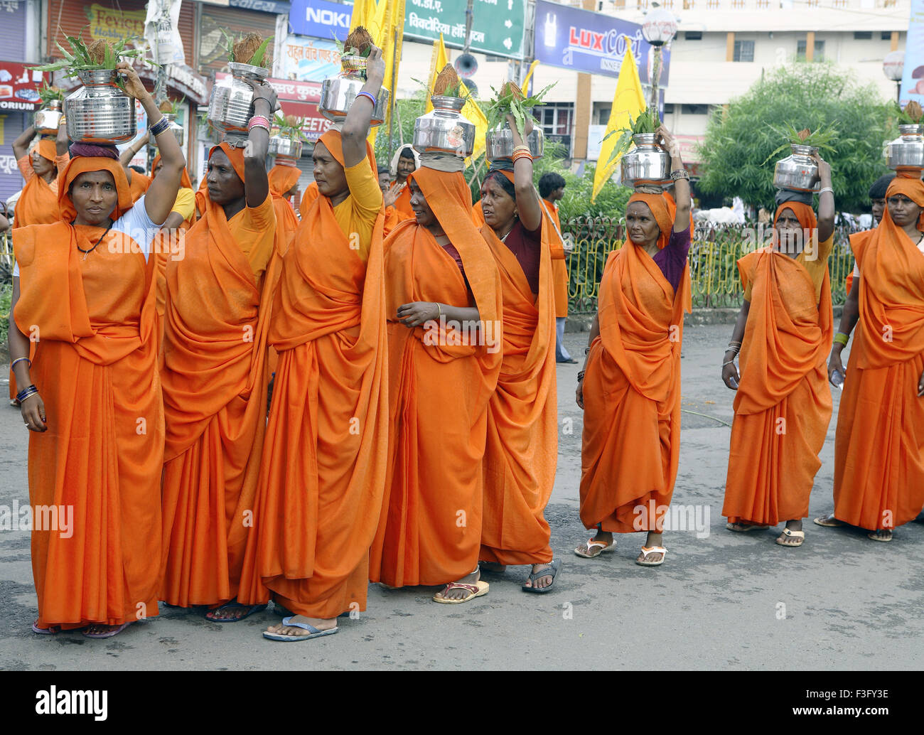 Janmashtami festival Lord Krishna birthday celebration carnival procession women dressed orange sari carrying steel Jabalpur Stock Photo