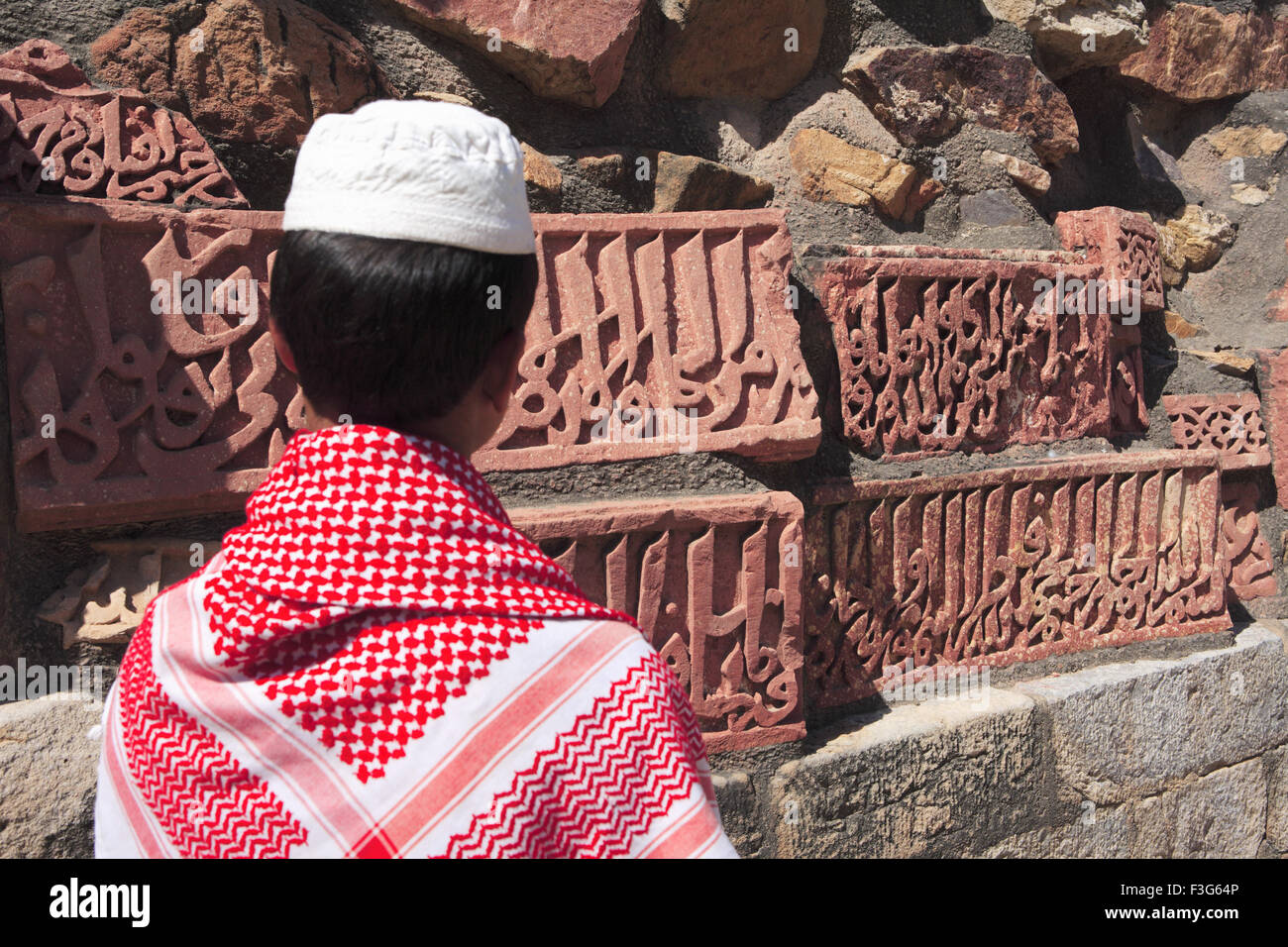 Muslim boy watching Islamic Ornamentation of Quran inscription carved Qutab Minar complex red sandstone Indo Muslim art Delhi Stock Photo