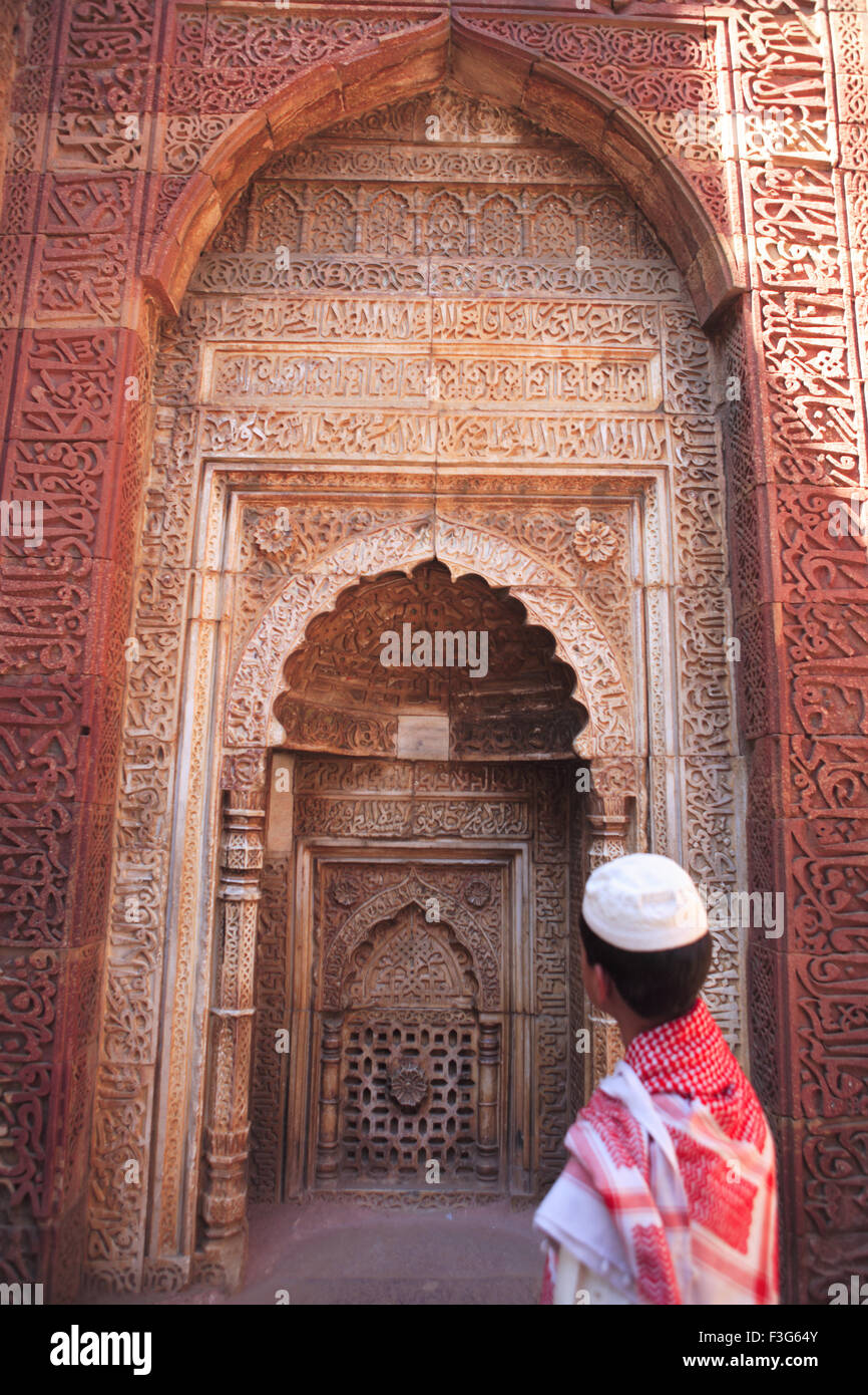 Muslim boy watching Islamic Ornamentation Quran inscription carved Qutab Minar complex red sandstone tower Indo Muslim Delhi Stock Photo