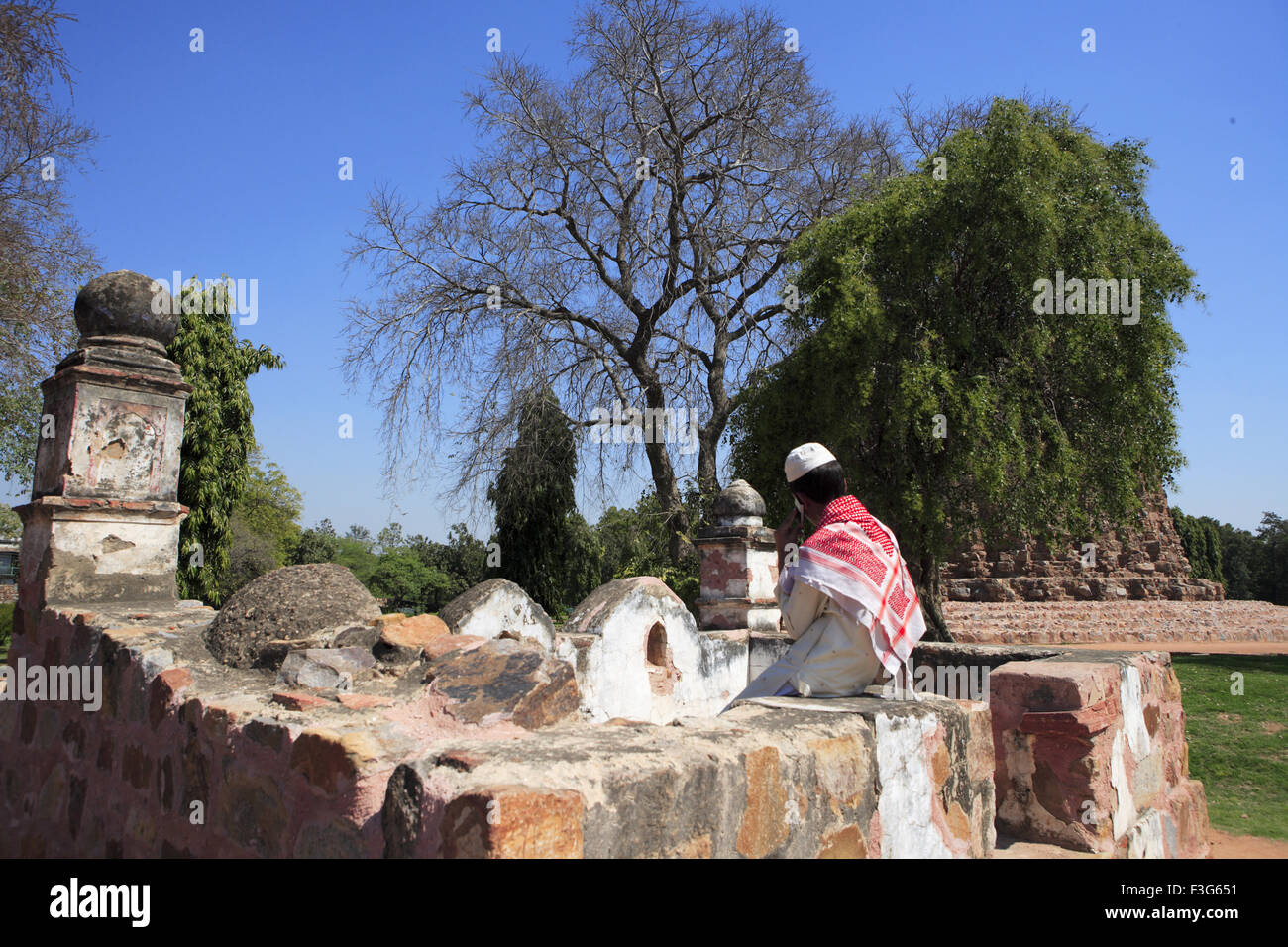 Muslim boy talking on mobile phone in Qutab Minar Complex ; Delhi sultanate ; Delhi ; India UNESCO World Heritage Site Stock Photo