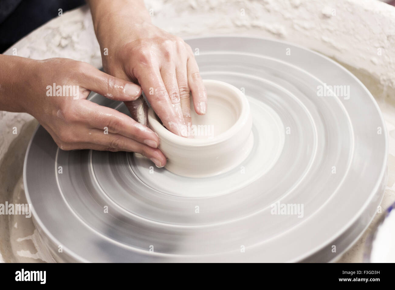 Potter creates a cup and saucer on the pottery wheel from raw white clay Stock Photo