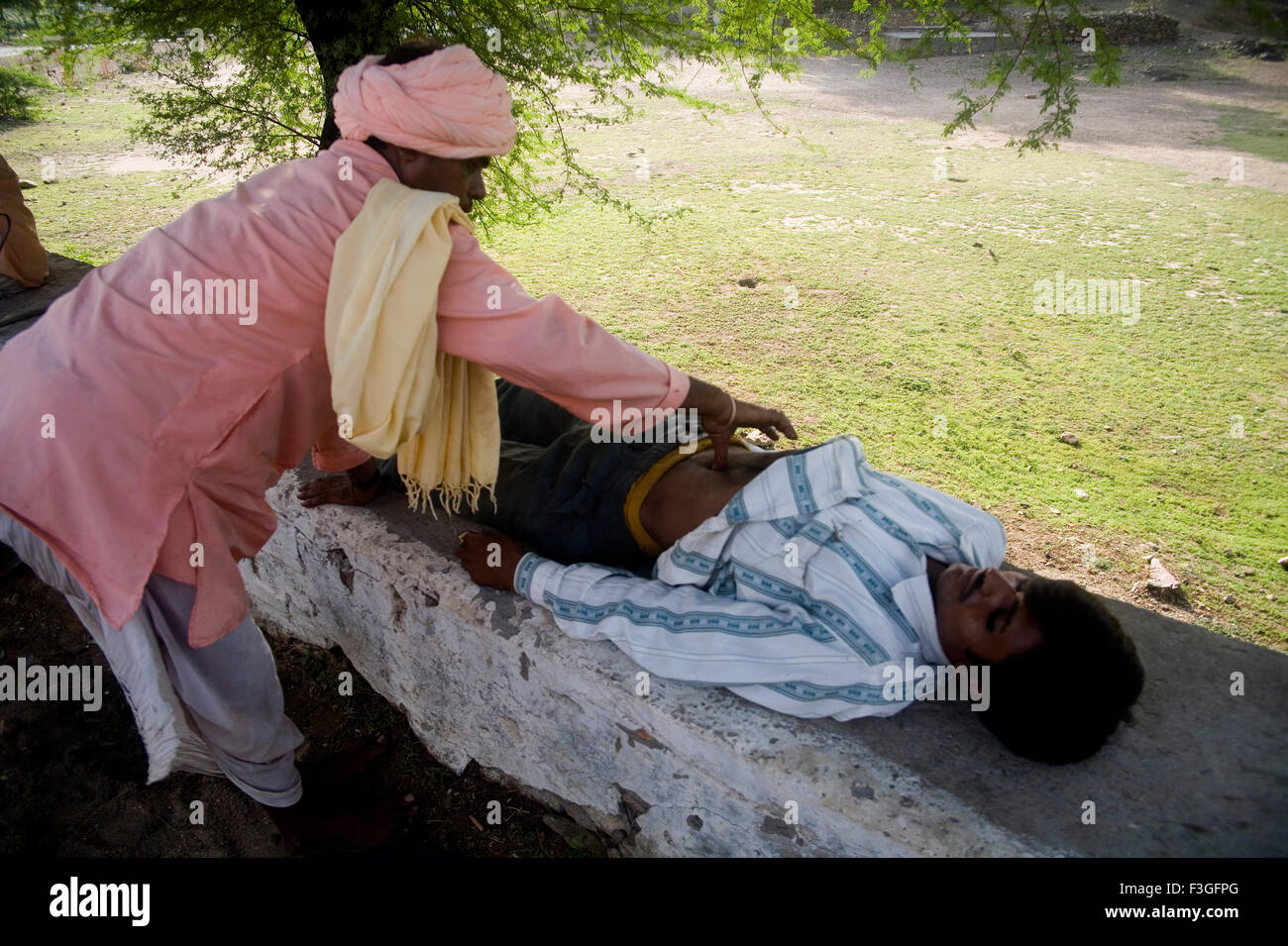 Traditional Indian male of Bheel community performing health check up of patient ; Village Delwada ; Udaipur ; Rajasthan Stock Photo