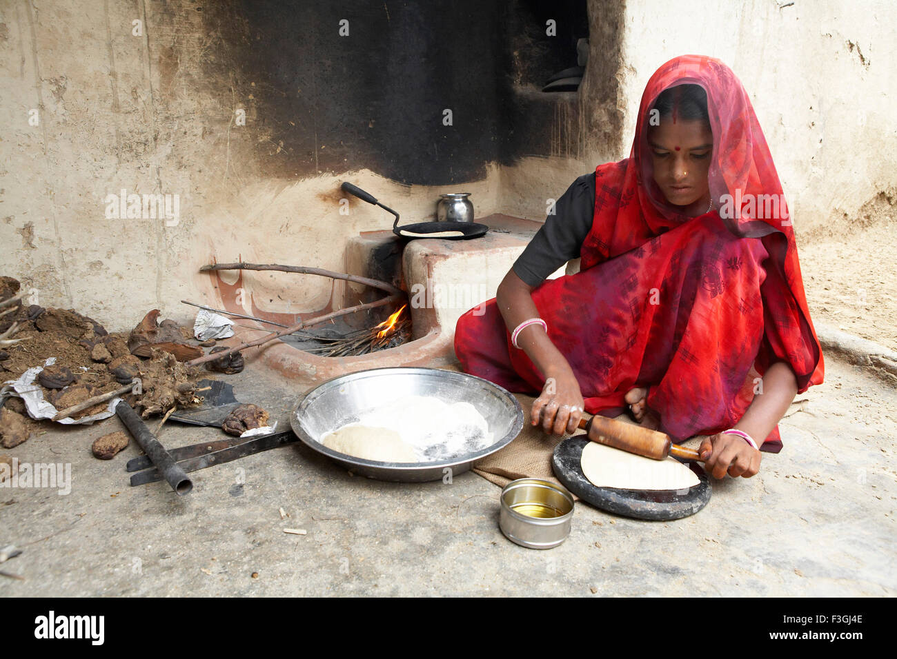 Indian woman making wheat bread or rotis by rolling pin on open ...