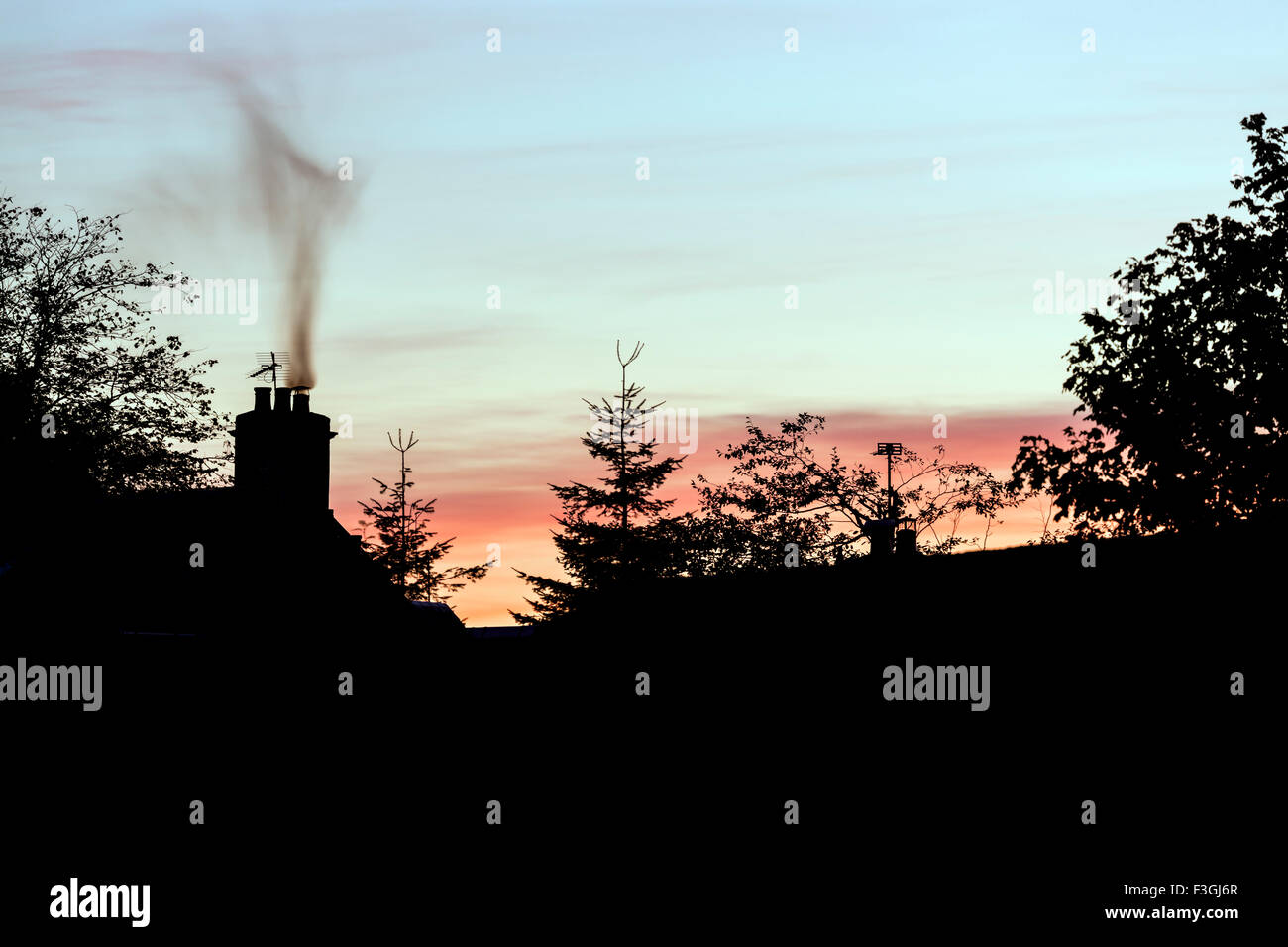 Smoke rising from a house chimney at sunset, UK Stock Photo