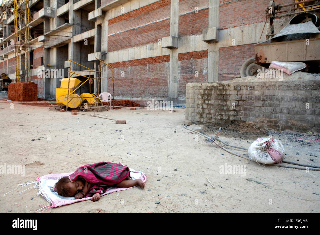 An unattended child sleeps on the construction site while her parents are busy working ; Ahmedabad ; Gujarat ; India Stock Photo