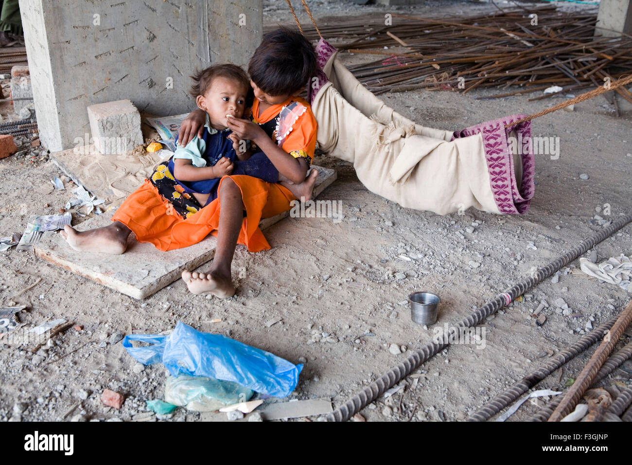 A young girl feeds her sibling at a construction site while their parents are away on work ; Ahmedabad ; Gujarat ; India Stock Photo