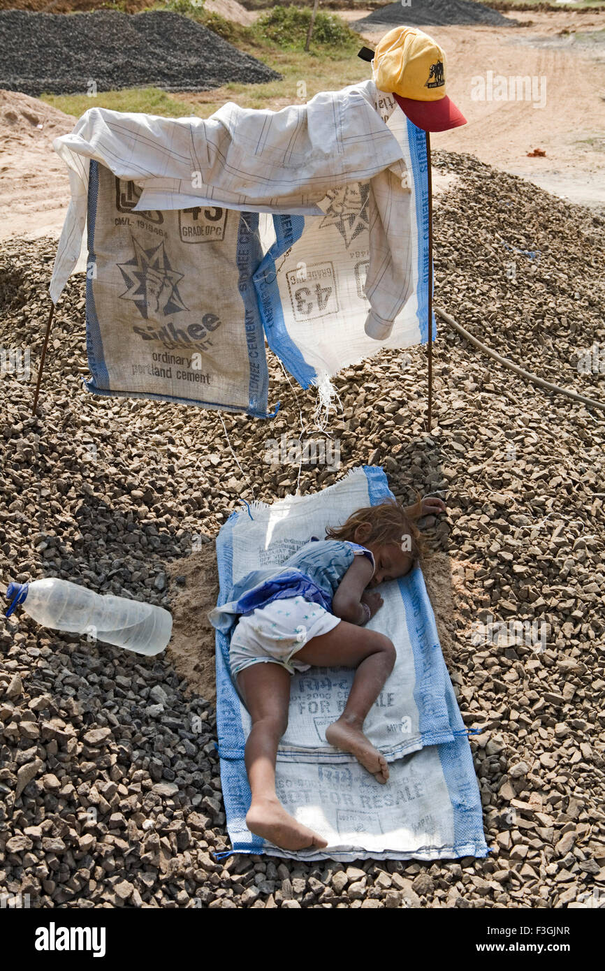 temporary shelter shades young girl sleeping gravel parents are away at work ; Ahmedabad ; Gujarat Stock Photo