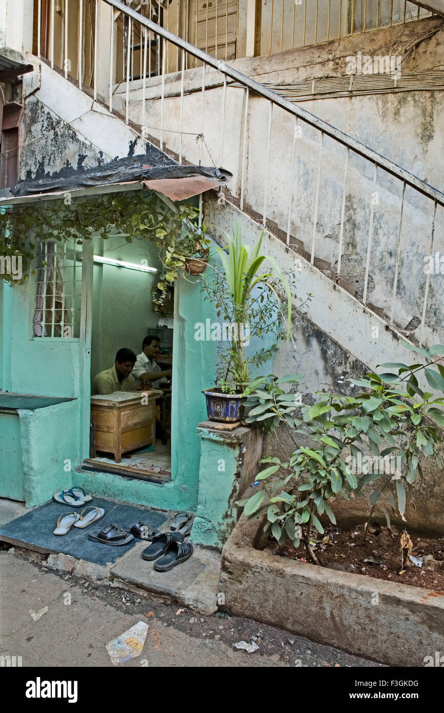 A repair shop owner finds a convenient space under the staircase of a building ; Mumbai Bombay ; Maharashtra ; India Stock Photo