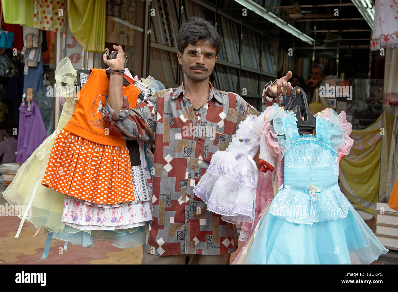 A hawker displays ready Indian dresses as he walks along a busy street ; Mumbai Bombay ; Maharashtra ; India Stock Photo