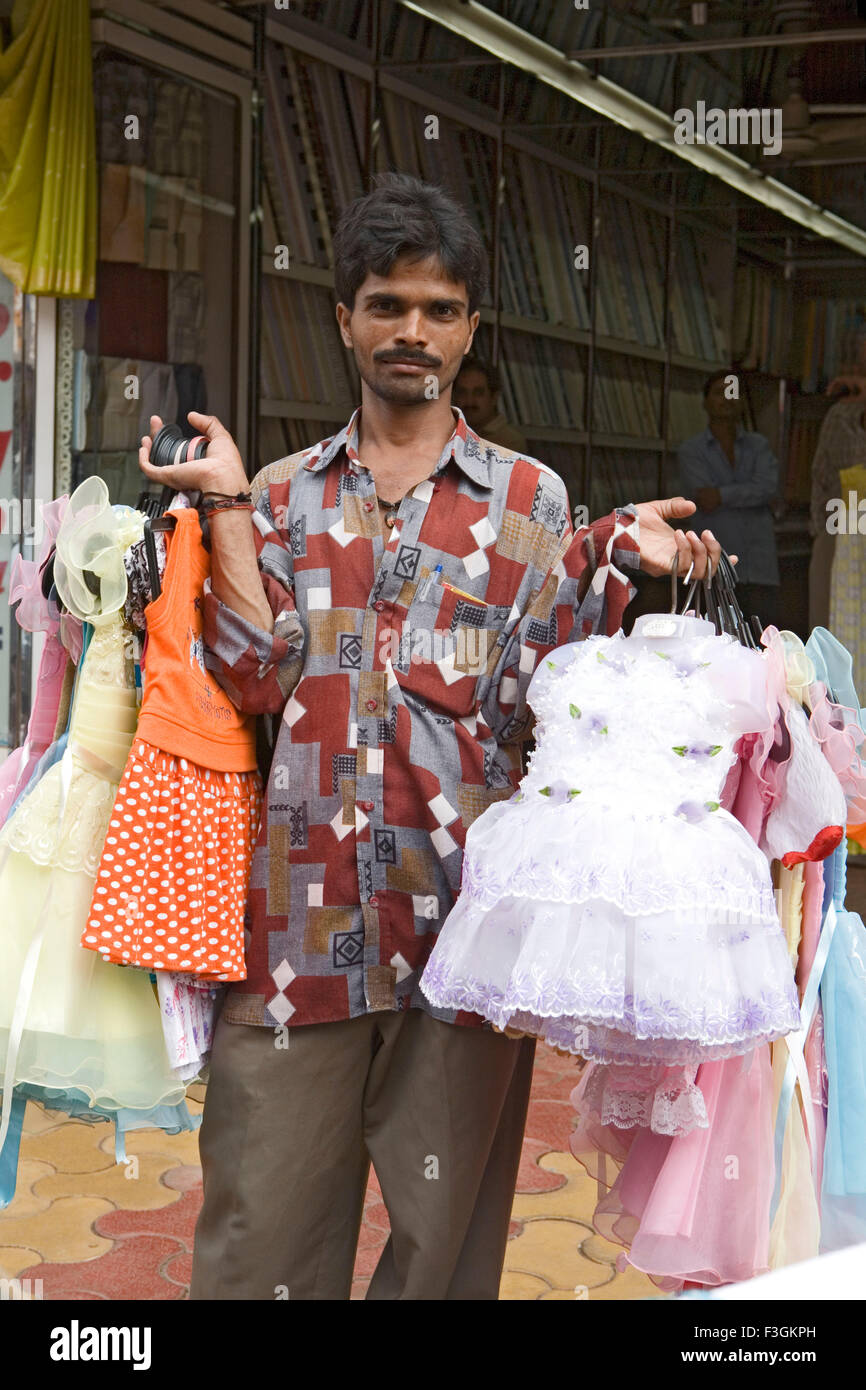 A hawkers displays in his hands a bunch of children's ready Indian dresses as he walks along a busy road ; Mumbai Stock Photo