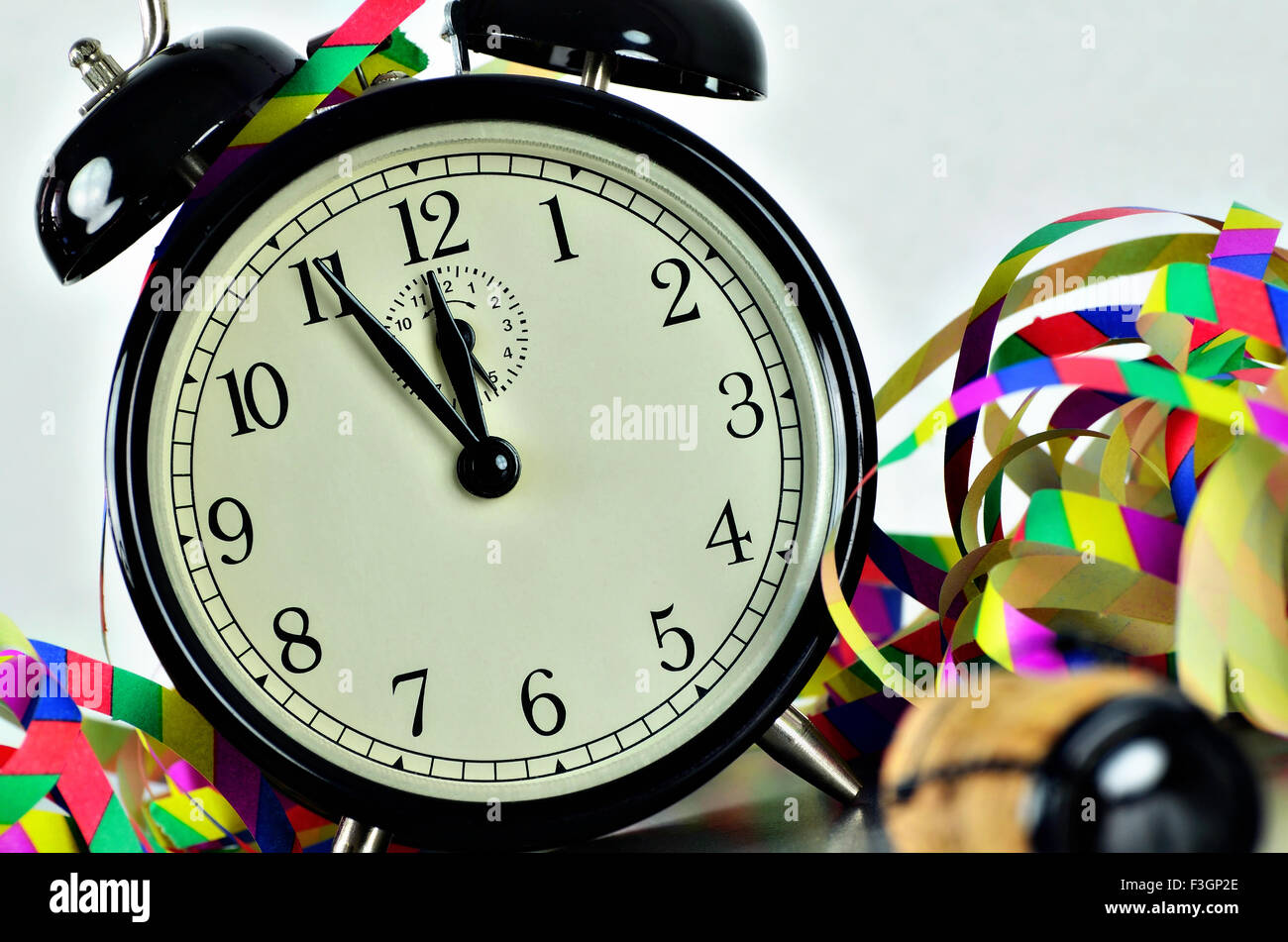 close up of  a black retro alarm clock, around midnight, with paper streamers and cork from a bottle of sparkling wine, slanted Stock Photo