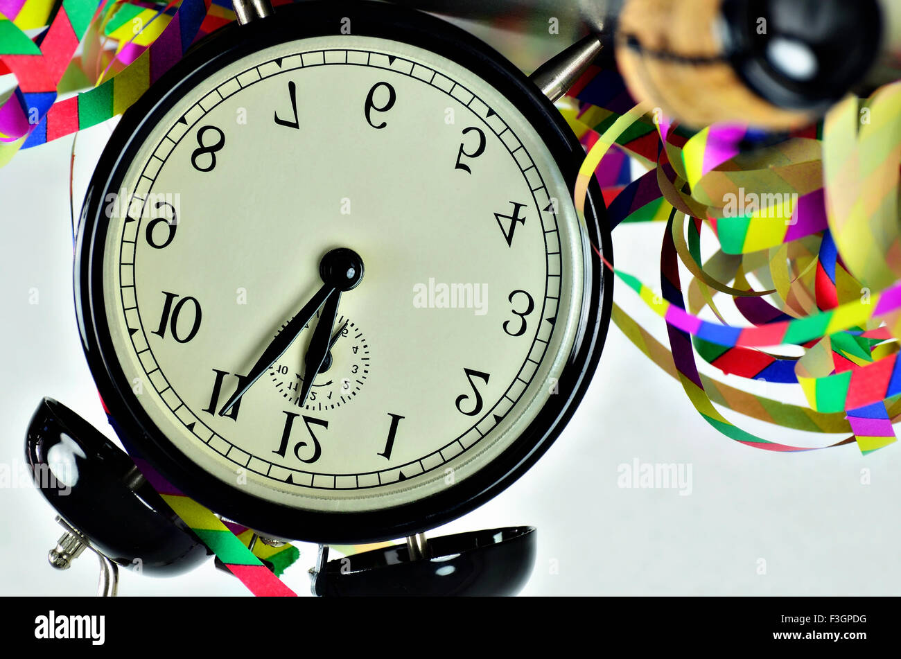 close up of  a black retro alarm clock, around midnight, with paper streamers and cork from a bottle of sparkling wine, headlong Stock Photo
