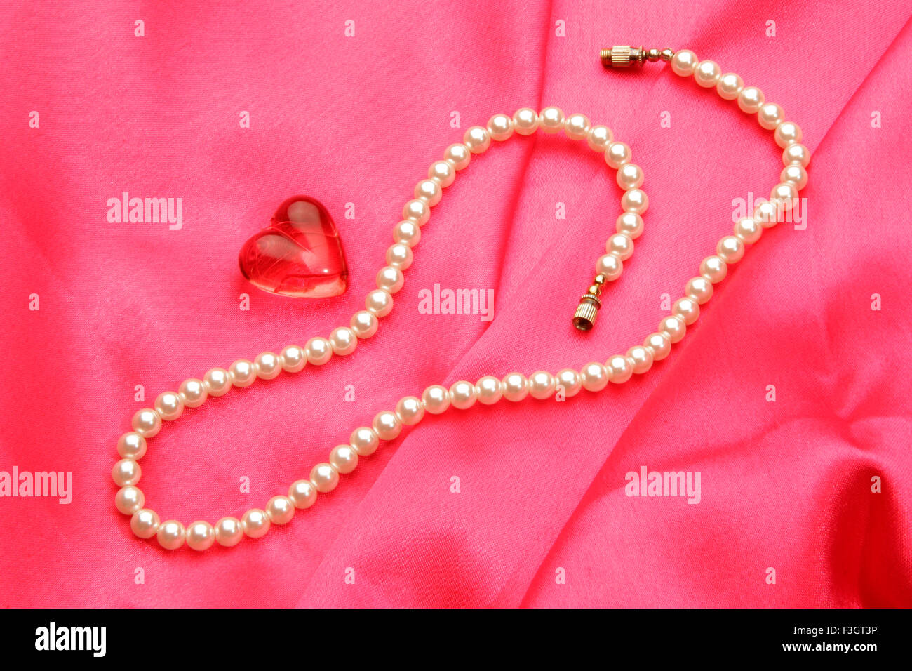 Jewellery in form pearl necklace with synthetic red gem stone of heart shape against pink satin background Stock Photo