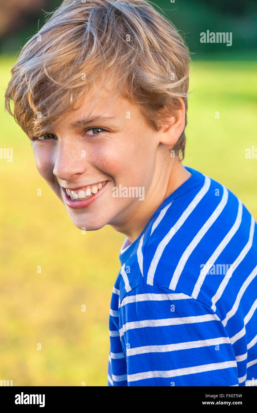 Young happy laughing male boy teenager blond child outside in summer sunshine wearing a blue striped t-shirt Stock Photo