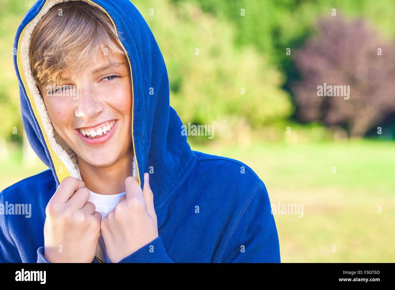 Young happy laughing male boy teenager blond child outside in summer sunshine wearing a blue hoody Stock Photo