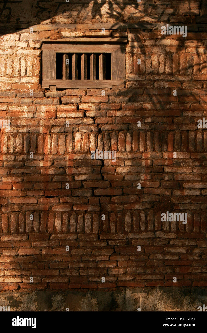 Abstract of bricked wall with lots of texture and small window having shadows of tree falling on ; Trambak Nashik Stock Photo