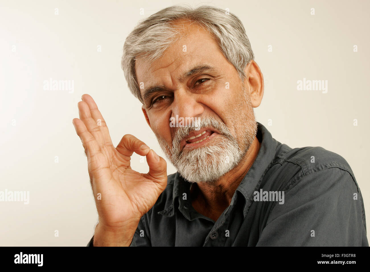man late fifties gray hair beard wearing blue shirt expressing indicating aggressively top hand finger thumb touching Stock Photo