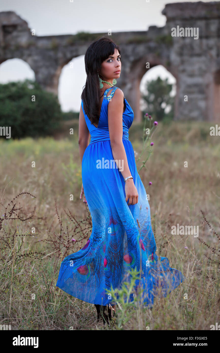 A brunette girl with an electric blue dress, taken in the scenery of the park of the ancient Roman aqueducts. Stock Photo