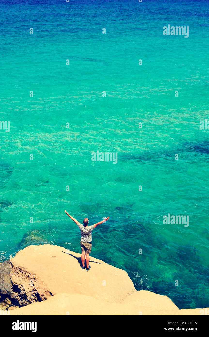 a young man with his arms in the air in front of the ocean, feeling free, with a filter effect Stock Photo
