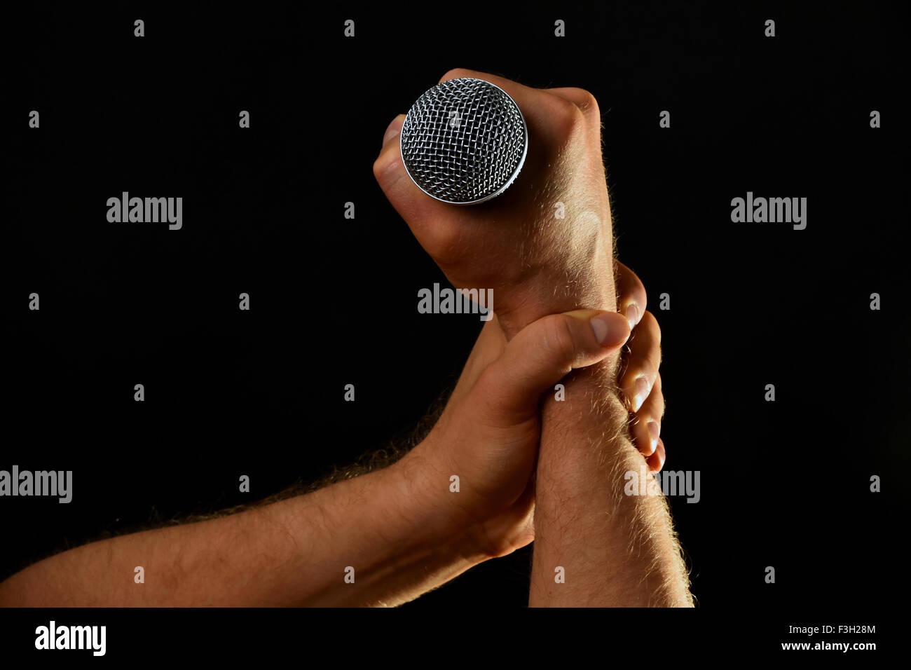 Two male hands holding microphone with wire cable isolated on black background Stock Photo