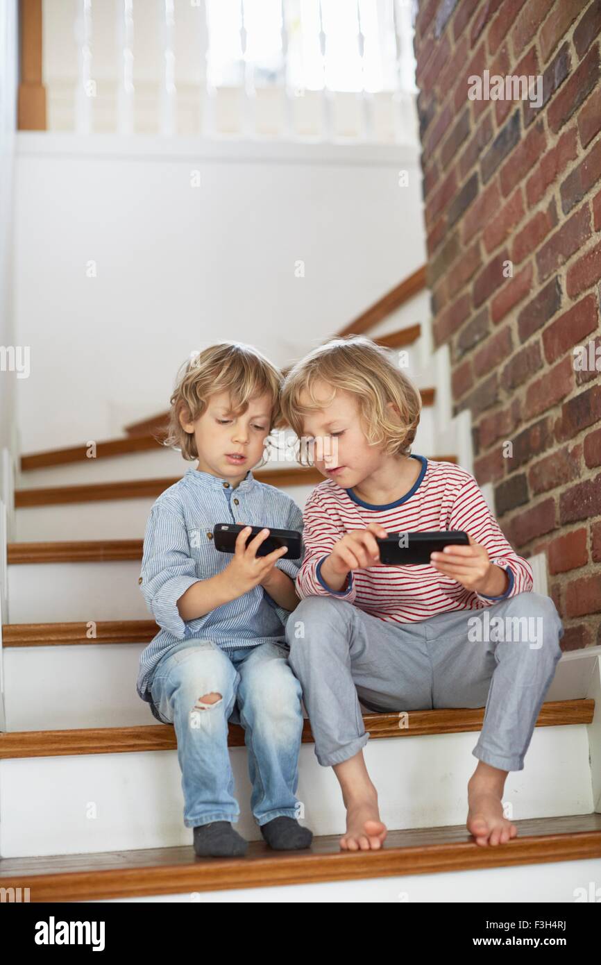 Two young boys, sitting on stairs, looking at smartphones Stock Photo