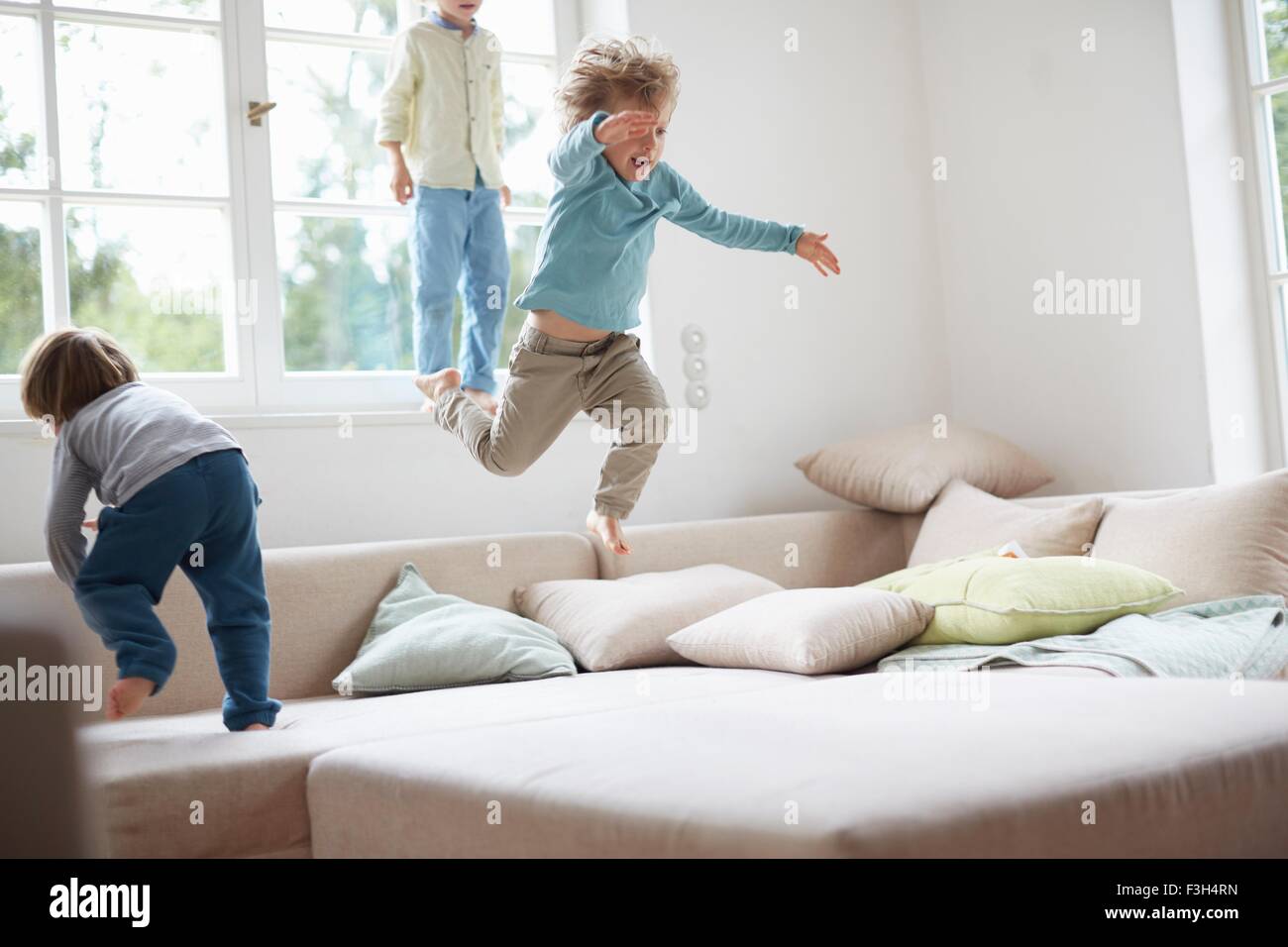 Three young boys jumping on sofa Stock Photo
