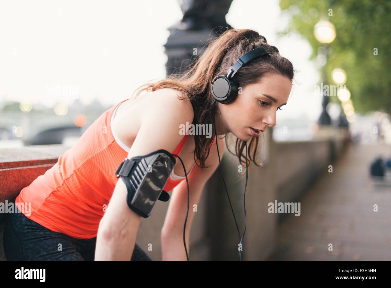 Exhausted female runner wearing headphones taking a break on riverside Stock Photo