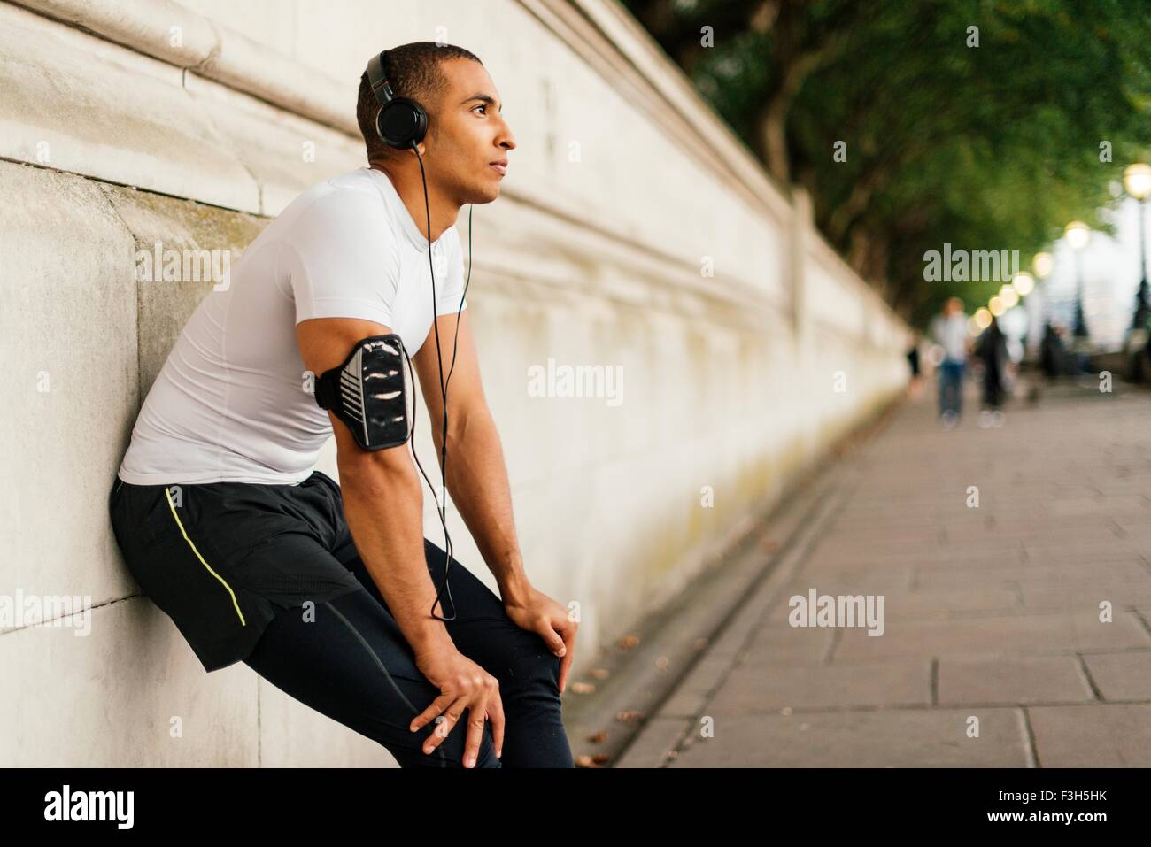 Male runner wearing headphones taking a break on riverside Stock Photo