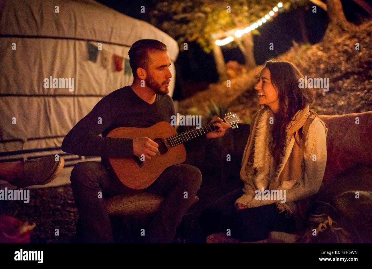 Young man serenading young woman with guitar next to yurt Stock Photo