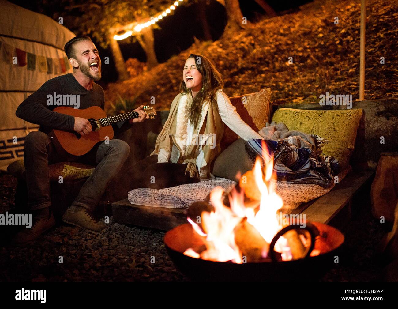 Young couple next to fire and yurt singing and playing guitar Stock Photo