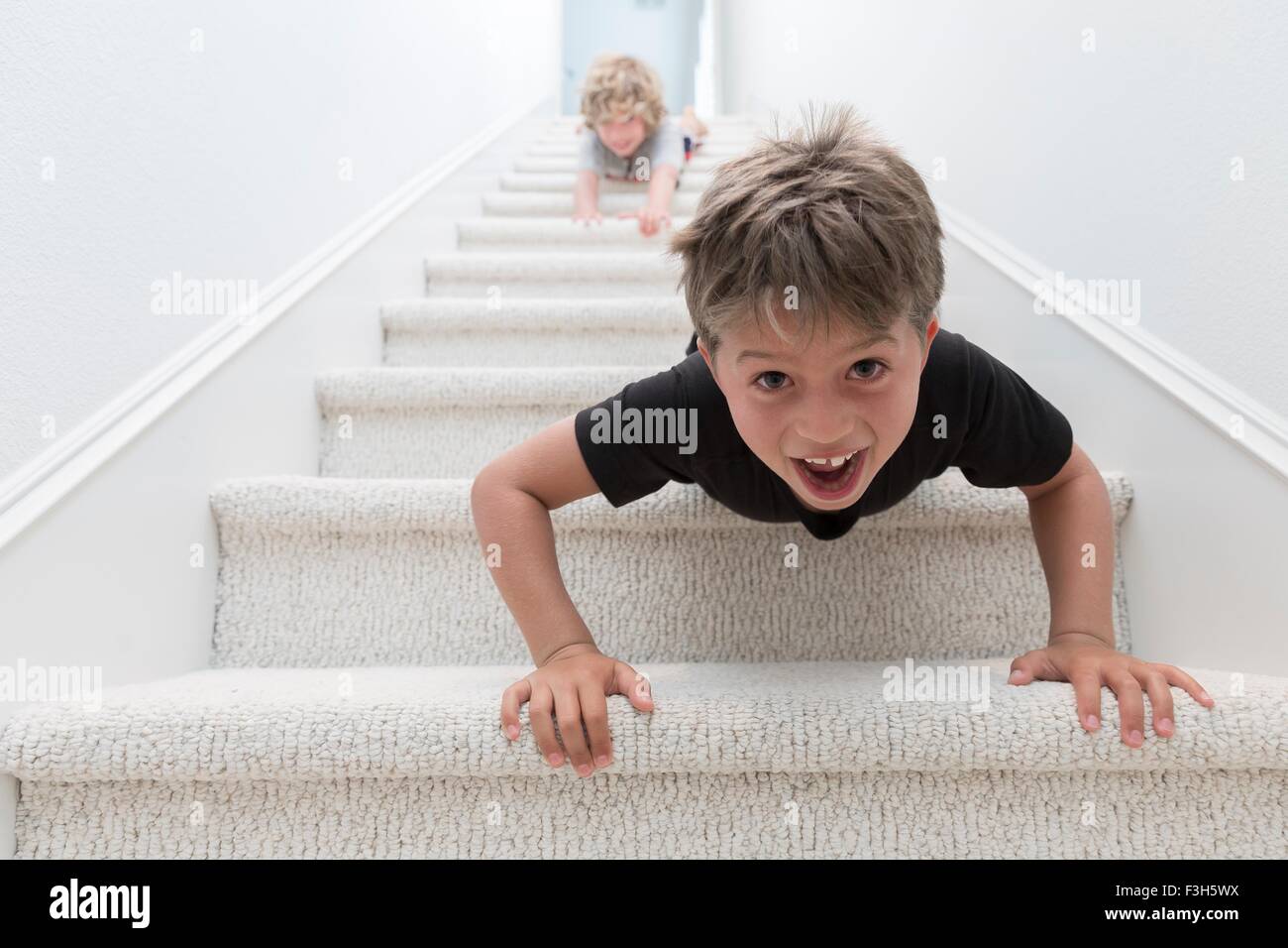 Portrait of two brothers crawling headfirst down stairs Stock Photo