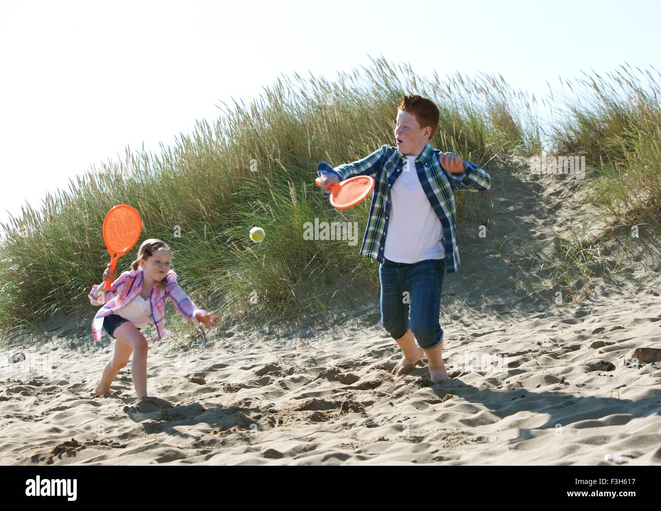 Girl and boy playing with orange sports bat and tennis ball on dunes Stock Photo