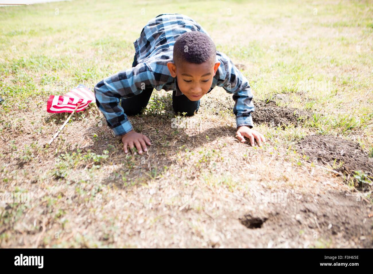 Boy crawling, peering into hole in ground Stock Photo