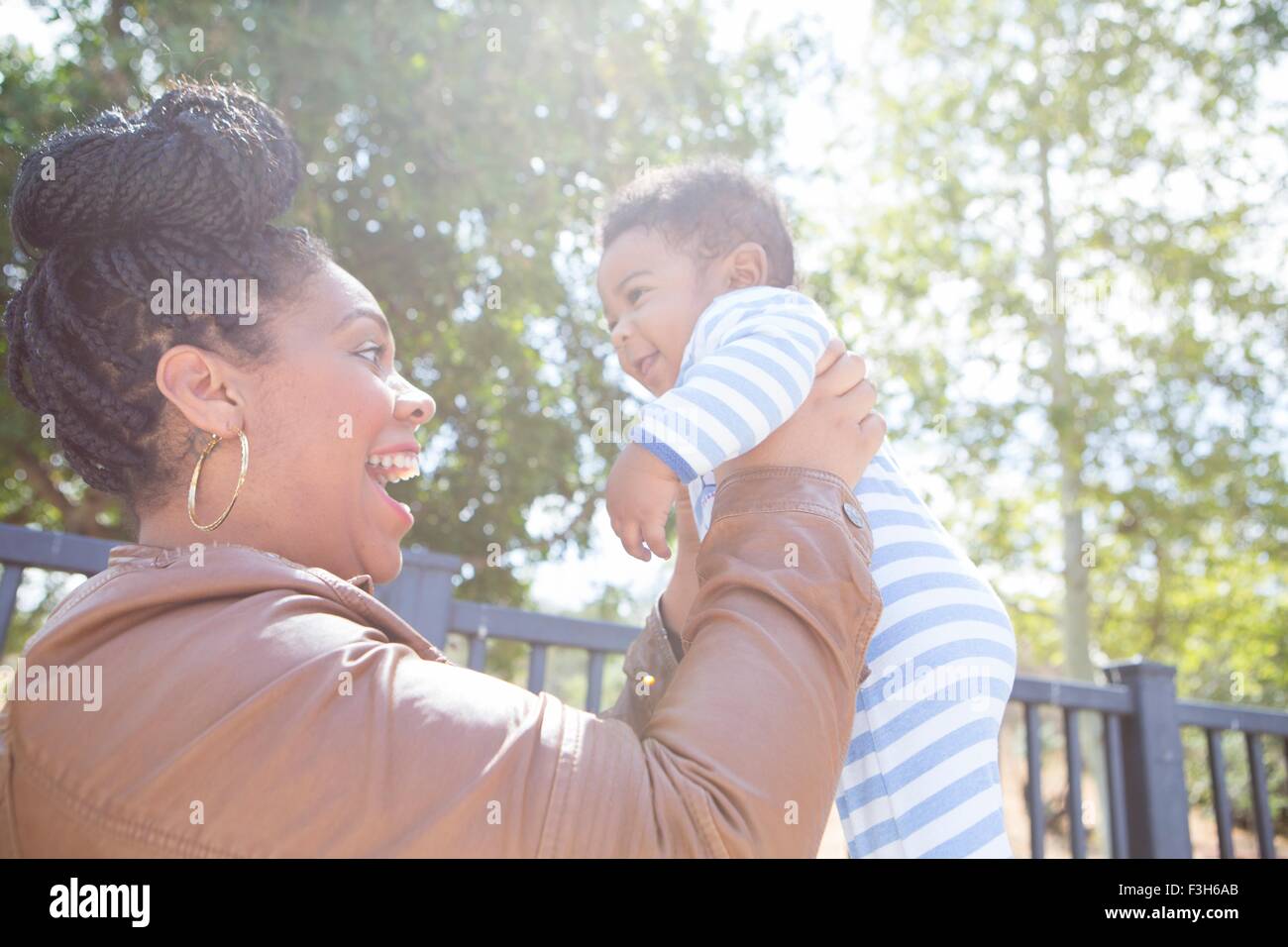 Mother holding up baby boy in park Stock Photo