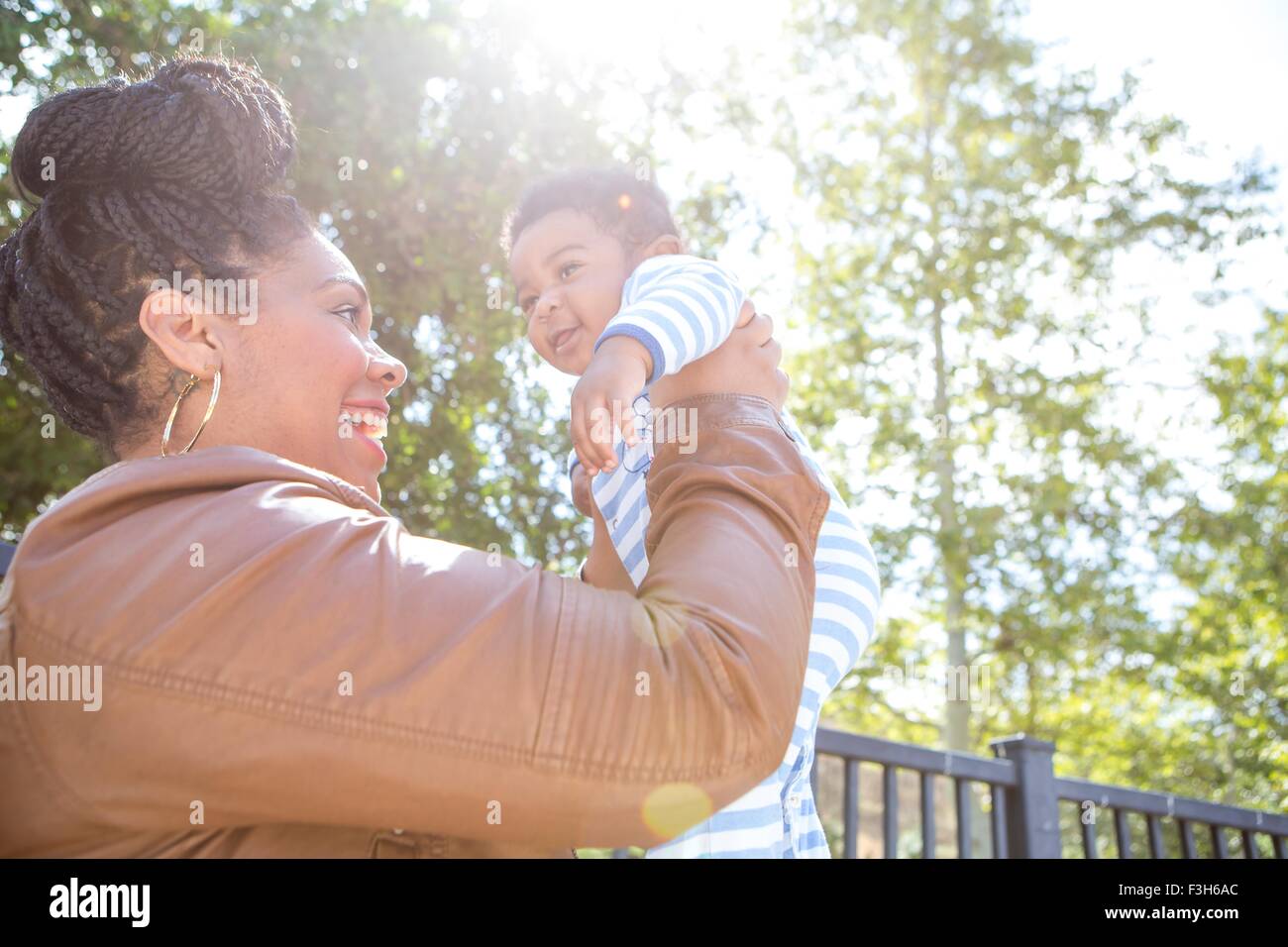 Mother holding up baby boy in park Stock Photo