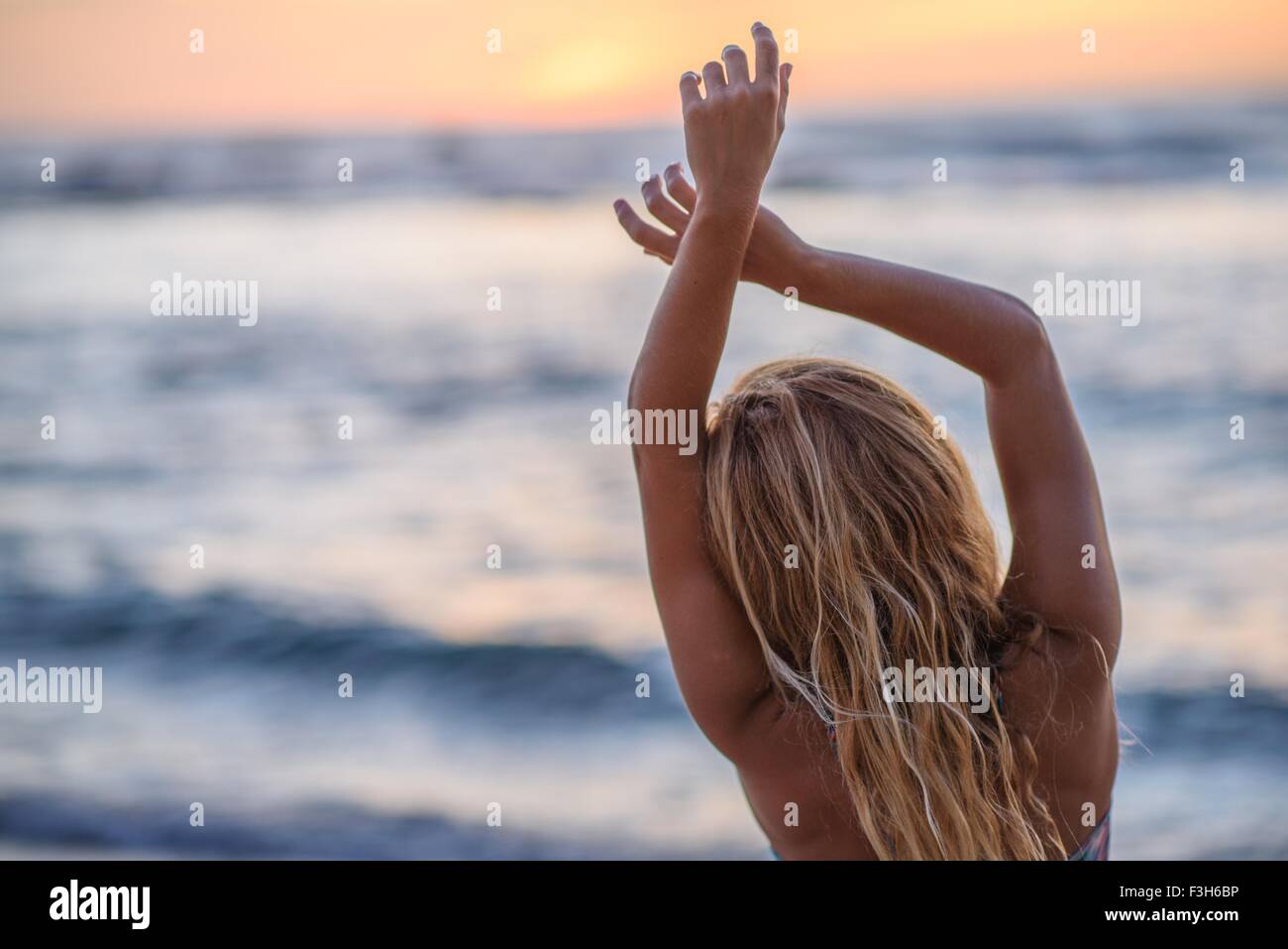 Rear view of young woman with arms raised on beach at sunset Stock Photo