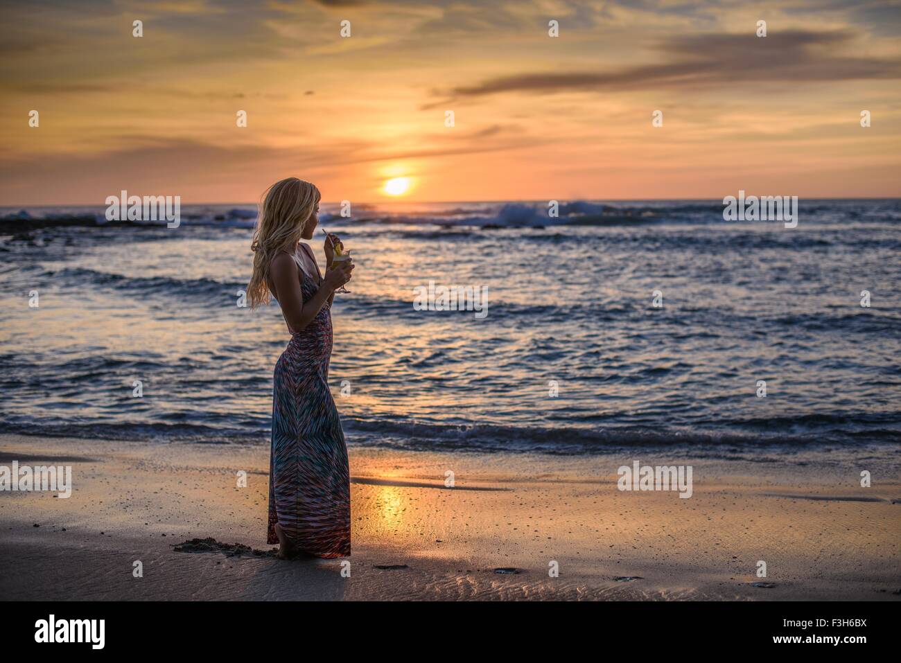 Young woman drinking cocktail on beach at sunset, Tamarindo, Costa Rica