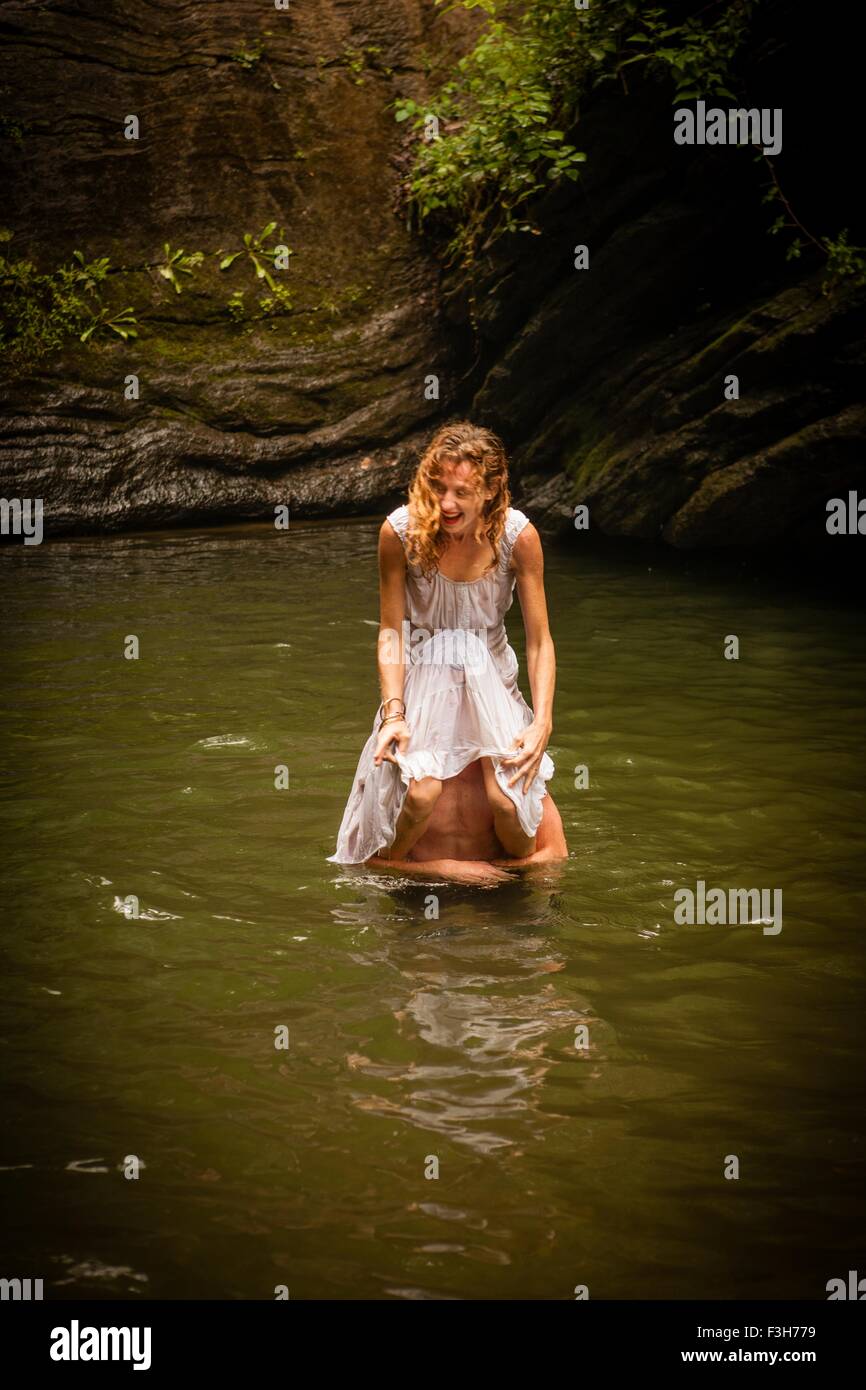 Mid adult woman wearing white dress sitting on shoulders of man in water laughing Stock Photo