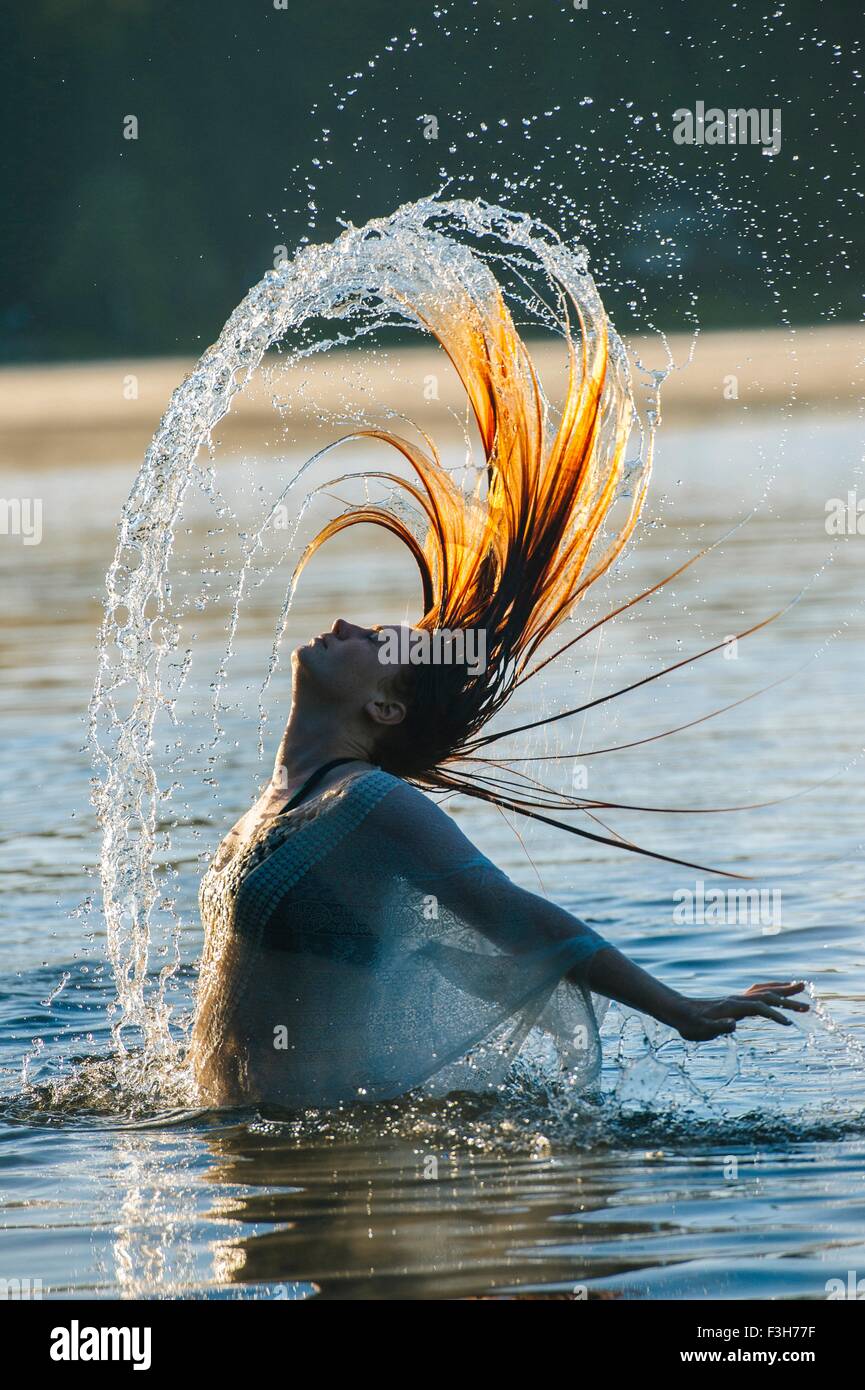 Side view of young woman in water throwing wet hair back arms open Stock Photo